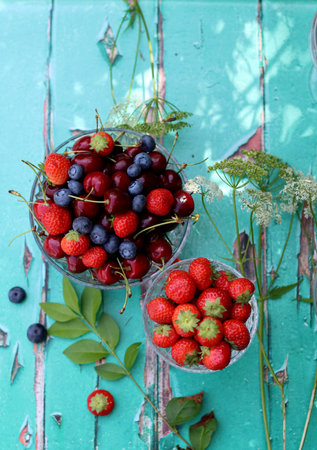 Glass bowls with fresh summer berries on old wooden table. Breakfast in the garden. Blueberry, strawberry, sweet cherry close up photo.の写真素材
