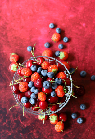 Fresh berries in a glass bowl on a red background, top viewの写真素材