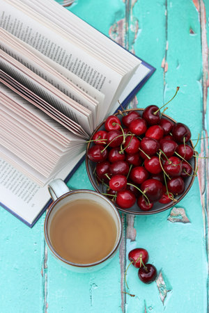 Cup of tea, books and cherries on turquoise wooden backgroundの写真素材