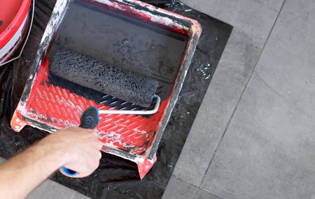 Painter's tools close up photo. Worker in the process of painting the wall with a paint roller. Paint roller in hand on a gray background, close-upの写真素材
