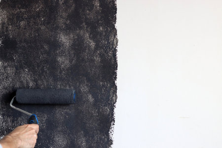 Male worker applies black paint on a white wall. Painting a wall with a roller in black and white colors.の写真素材
