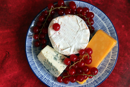 Cheese plate with red currant and blue cheese on red backgroundの写真素材