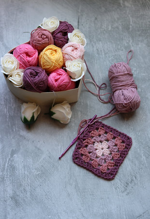 Knitting wool balls and crocheted flower on grey background.