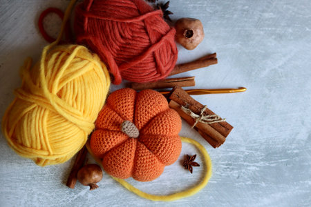 Crochet pumpkin with woolen threads and cinnamon sticks on grey background