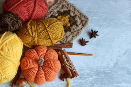 Knitted pumpkin with woolen threads, cinnamon and anise on gray background