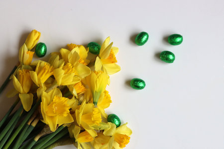 Yellow daffodils and green chocolate easter eggs on white background