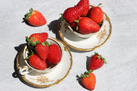 Strawberries in a porcelain cup on a light grey background with space for text. Still life photo with retro tableware and summer fruit. Eating fresh concept.の写真素材