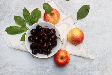 Ripe cherries and apples in a bowl on a light backgroundの写真素材