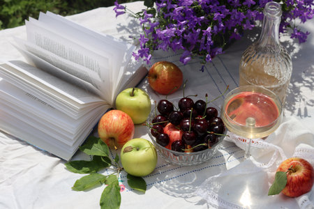 Summer picnic in the garden. Apple, cherry, wine and book.の写真素材