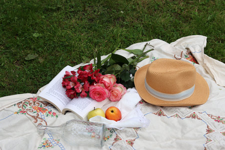 Bouquet of roses, apples, hat and book on the grass