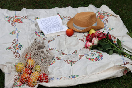 Bouquet of tulips, apples, a hat and a book on a picnic blanket