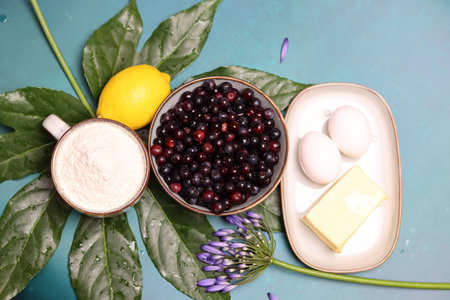 Ingredients for cooking berry pie. Milk, cottage cheese, butter, berries, lemon, mint leaves on blue...