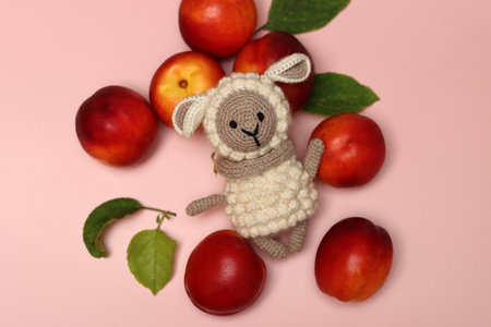 Knitted toy sheep with peaches and leaves on a pink backgroundの写真素材