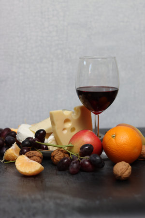 Glass of red wine, grapes, cheese and fruits on a dark backgroundの写真素材