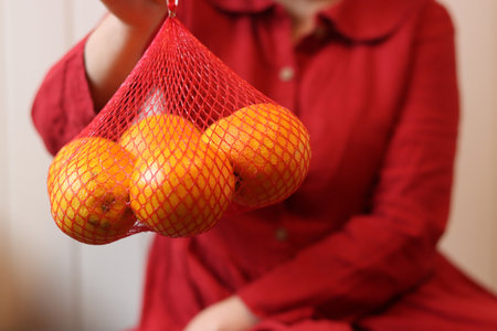 Woman in red dress holding oranges in a mesh bag, closeupの写真素材