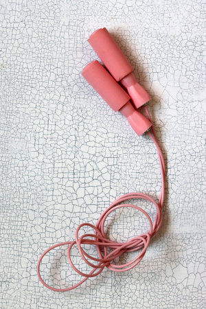 Pink jumping rope on cracked white background. Top view with copy space