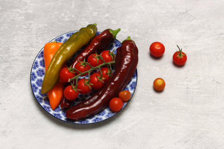 Red and yellow peppers and cherry tomatoes on a blue plate on a light backgroundの写真素材