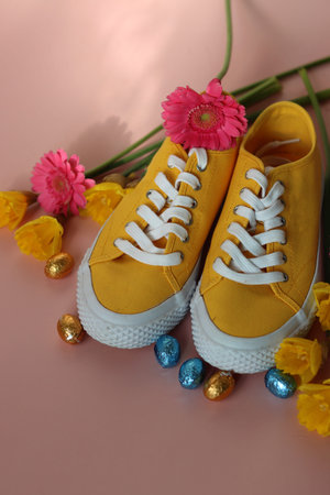 Yellow sneakers with flowers and easter eggs on a pink background.の写真素材