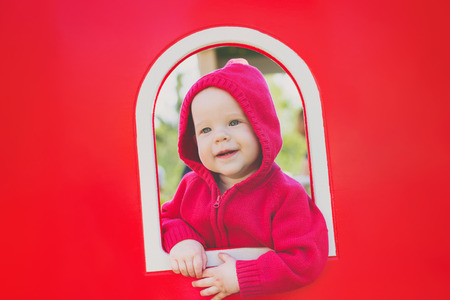 A cute toddler is peeking out of the window in the playground.の写真素材