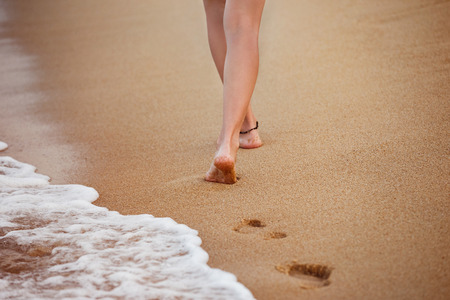 Healthy young woman is walking on the yellow sand leaving footprints.の写真素材