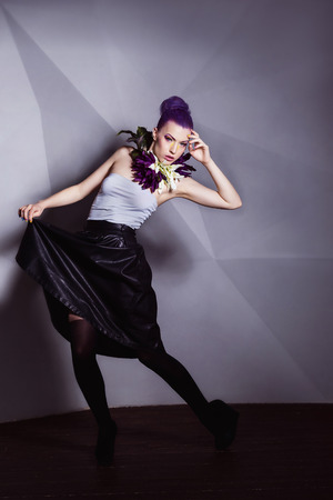 A young model with flowers on her neck is posing near the grey wall background.の写真素材