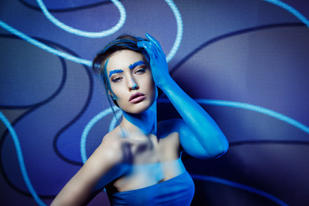 Close-up fashion image of a beautiful woman with blue colour body art and unusual wall at background.の写真素材