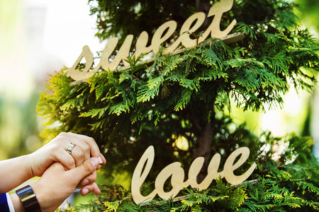 Wedding and love concept. Two hands holding at handmade wooden word sweet love background.の写真素材