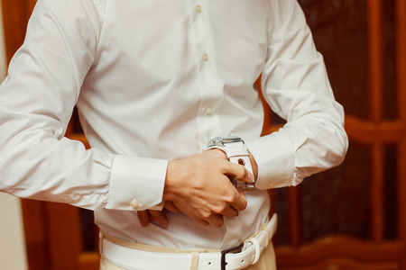 Close-up image of a man in white shirt who fastens a clock. Concept of a young man morning.の写真素材