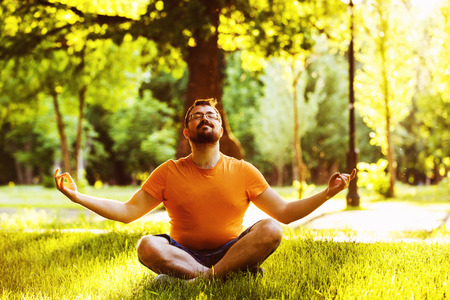 A happy thoughtful dreamer man is sitting on green grass in a park at sunny summer day and looking into future. Concept of relaxation, wellbeing, lifestyle.の写真素材