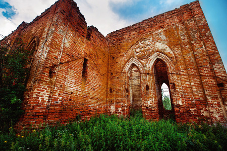 Beautiful view of old ruined red bricks church with arches at summer green grass and blue sky  background.の写真素材