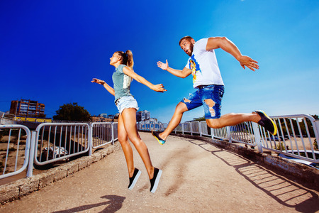 Funny young couple is jumping catching each other outdoors at summer bright blue sky background.の写真素材