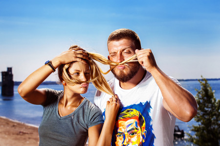 Couple of young joyful sexy girl and bearded man playing with hair as fake mustache at summer outdoors background.の写真素材