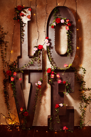 Word love made with big metal letters decorated with flowers at wall background.の写真素材