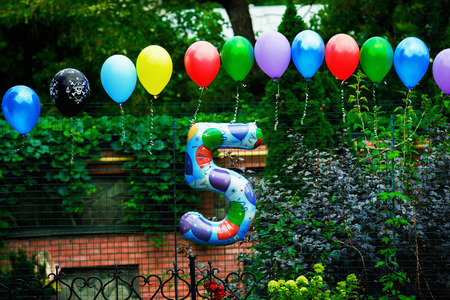 Green summer park decorated for colorful birthday party with baloons having shape of number five.の写真素材