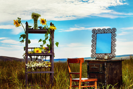 Beautiful rural landscape of field with vintage furniture decorated with wild flowers at blue summer sky background.の写真素材
