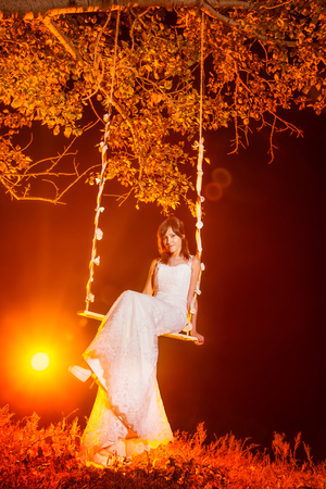 Beautiful happy bride is swinging outddors at bright red light background.の写真素材