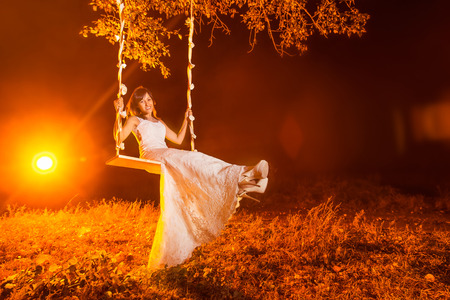 Beautiful happy bride is swinging outddors at bright red light background.の写真素材