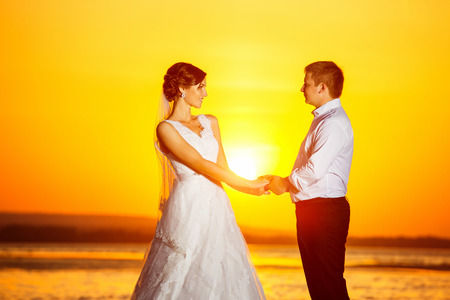 Young man is holding his beautiful bride's hand at amazing tropical sea sunrise background.の写真素材