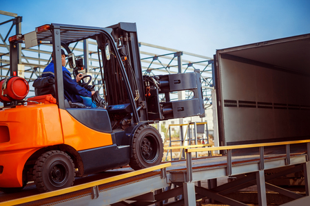 Forklift is putting cargo from warehouse to truck outdoorsの写真素材