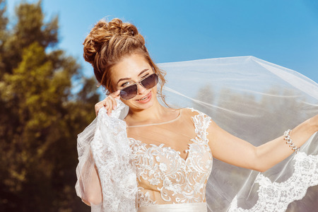 Closeup portrait of beautiful smiling bride in sunglasses at summer outdoors background.の写真素材
