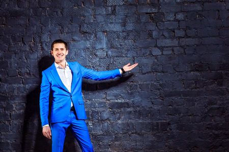 Happy young man in suit is pointing at wall background making promotion.の写真素材