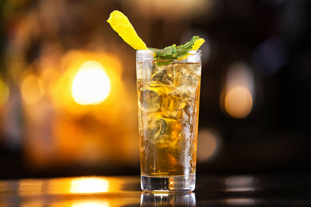 Closeup glass of long island ice tea cocktail decorated with mint at orange lighted bar counter background.の写真素材