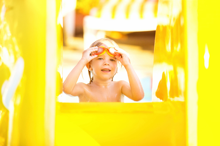 Cute child is standing at slide in swimming pool and holding glasses.の写真素材