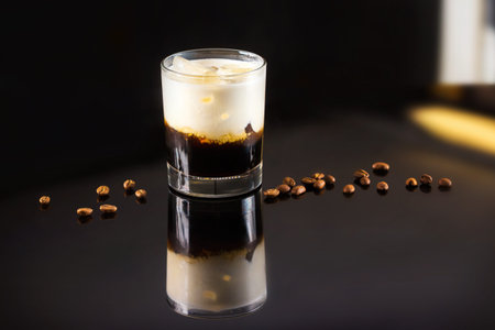 Closeup image of glass of black Russian cocktail and coffee beans at dark bar stand background.