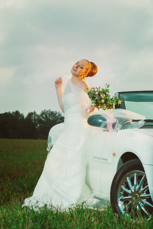 Vertical portrait of happy bride sitting on a car outdoors at field background.の写真素材