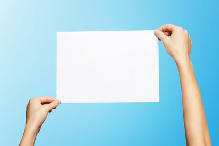 Mockup of female hands holding blank paper list isolated at blue background.の写真素材