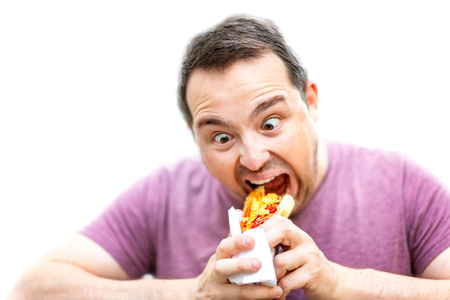 Hungry man with crazy eyes is eating hot dog isolated at white background.の写真素材