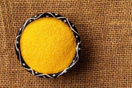 Closeup top view bowl of raw polenta corn at left corner of sack cloth background.の写真素材