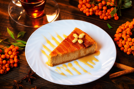 Closeup image of cheesecake slice decorated with maple syrup, cup of tea and rawan branches at wooden board background.の写真素材