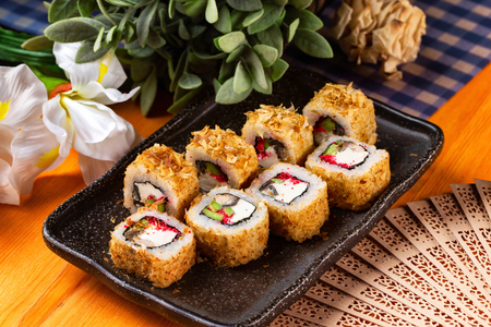 Plate of tempura maki sushi rolls with cream cheese, avocado and tuna at decorated with flowers table background. Plate of tempura maki sushi rolls with cream cheese, avocado and tuna at decorated with flowers table background.